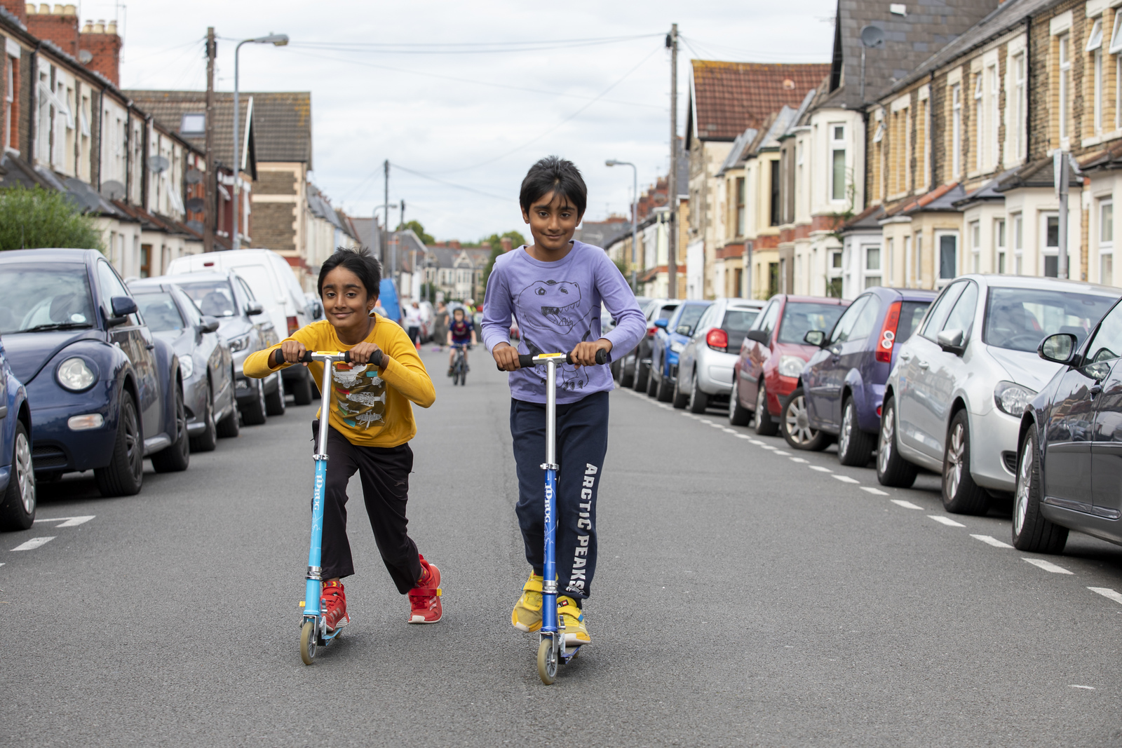 Two young children scootering down a street that is closed to traffic